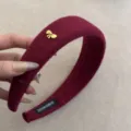 Detalle de diadema acolchada de lana granate con adorno de lazo dorado fino. - Burdeos