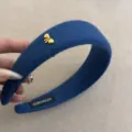 Primer plano de una diadema de lana azul con un lazo dorado y etiqueta de hecho a mano - Azul