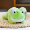 Lindo peluche de rana verde claro en posición tumbada sobre un mantel de paja trenzada - Rana / 20cm