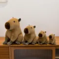 Cuatro peluches de capibara de varios tamaños exhibidos en un mueble de madera rústica - Dijes / 12cm / Café