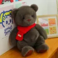 Soft brown plush teddy bear toy wearing a cozy red knitted scarf displayed on a wooden shelf - Red Scarf Style / 45 cm