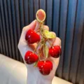 Llavero de cerezas rojas brillantes con hojas doradas sostenido a mano - Cereza (Colgante de Cereza de Fruta) / Cereza Roja