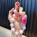 Hand houdt een schattig roze kralen telefoonkoordje vast met een zeeschelp hanger - Roze / Inclusief Pakking
