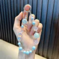 Hand houdt een lichtblauw iriserend kralen telefoonkoord met ster- en roosbedeltjes voor tassen - Blauw