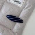 Dettaglio di molletta per capelli in tessuto a righe blu navy e bianco su fondo neutro - Fermaglio ovale / Saia Blu