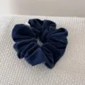 Detail view of a navy blue velvet scrunchie on a white textured fabric background. - Dark Blue