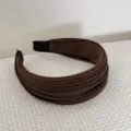 Vue détaillée d'un serre-tête large plissé marron sur un fond en tissu texturé. - Brun Foncé
