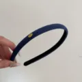 Macro view of a navy blue suede headband featuring a gold 'Love' engraved plate detail. - Dark Blue