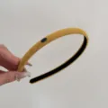 Close-up detail of a mustard yellow suede thin headband with a small blue decorative plaque - Yellow