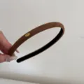 Macro view of a minimalist brown suede headband with a decorative gold Love tag detail - Brown
