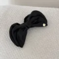 Detailed view of an elegant black fabric bow banana hair clip with a golden brand tag - Bow Banana Clip / Black