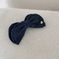 Macro detail of a dark blue denim bow banana clip with a gold metal brand tag - Bow Banana Clip / Dark Blue
