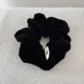 Close-up of a premium black velvet scrunchie featuring a decorative white fabric bow tag. - Black