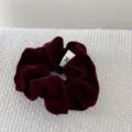 Close-up of a vintage burgundy velvet scrunchie with a minimalist white logo tag. - Red
