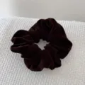Detailed top view of a coffee brown velvet scrunchie on a white textured background - Coffee