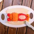 Cute orange and red plush lobster keychain lying on a white toy plate with wooden props. - Mantis Shrimp