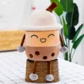 Adorabile peluche boba tea sorridente con cappello seduto su un cesto di vimini rustico - Tazza di Tè al Latte (Occhi Socchiusi) / 20cm