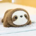 Adorable mini brown and white sloth plush toy resting on a white computer keyboard - Sloth