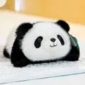 Cute palm-sized panda plush toy with soft black and white fur lying on a keyboard - Panda