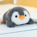 Adorable grey and white plush penguin toy resting on a white computer keyboard - Penguin