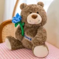 Adorable brown teddy bear plush toy holding a blue flower on a pink checkered chair. - Height Approx 28cm / Brown (Blue Flower Style)