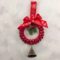 Detailed view of a festive red Christmas bell wreath featuring a pine cone and brass bell - Diameter approx 12cm / Red