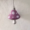 Detail showing a purple mushroom ornament with white spots and silver hanging string. - Purple