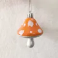 Close-up view of orange painted mushroom ornament with white spots and silver chain - Orange