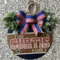 Patriotic July 4th wooden door sign with burlap bow and artificial greenery detail - Star Stripes Family Style
