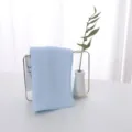Close-up of a soft light blue latex square face towel displayed on a minimalist gold stand - 30*30cm / Blue