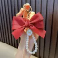 Handcrafted red ribbon bow keychain with elegant pearl bead strap and gold charm - Red