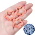 Close-up of hollow star charms with glitter, glowing light blue in dark conditions. - Luminous Orange