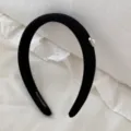 Close-up of a black ribbed headband featuring an elegant pearl heart detail on white fabric - Black