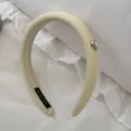 Close-up of cream textured padded headband with a heart-shaped pearl charm accent. - Yellow