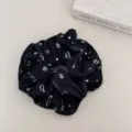 Detailed shot of black scrunchie with white floral print on a textured background. - Waist-Curve Hair Scrunchy / Black Bow
