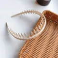 A close-up detail view of a beige minimalist long-tooth plastic headband on a rattan tray - White