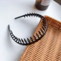 Detailed view of a flexible black plastic headband with long teeth on a woven tray - Bright Black
