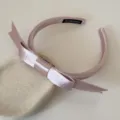 Detalle de una diadema rosa de raso con lazo sobre un soporte de piedra decorativo - Rosa