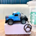 Blue miniature pullback toy truck keychain with decorative flame decals on a pink stand - Blue