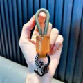 Hand holding a military green braided rope keychain with brown leather patch and black rings - Dark Green