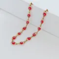 Primo piano delle perle rosse in vetro Evil Eye su catena a maglie dorata in acciaio - Catena Color Acciaio / Rosso