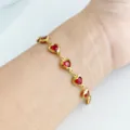 Dettaglio ravvicinato di un bracciale in acciaio dorato con gemme rosse a forma di cuore - Rosso