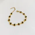 Close-up view of a gold stainless steel heart bracelet with black enamel centers - Black