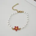 Dettaglio di bracciale in acciaio dorato con perle finte bianche e ciondolo a margherita - Colore acciaio / Rosso