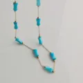Macro view of bright blue bamboo-shaped beads on a delicate gold stainless steel chain necklace - Lake Blue