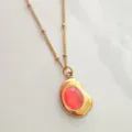 Detailed close-up of a gold-plated stainless steel necklace with a translucent red pendant - Orange Red