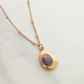 Detailed close-up of a vintage gold-plated necklace with a purple cabochon stone pendant. - Purple