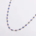 Dettaglio macro della collana in acciaio dorato con ciondoli hamsa evil eye smaltati - Oro / Blu