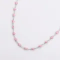 Primo piano di una collana in acciaio inox con perle rosa a forma di mano Hamsa. - Colore acciaio / Rosa