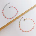 Dettaglio di bracciali in acciaio inossidabile con delicati ciondoli a cuore in smalto rosa - Oro / Rosa